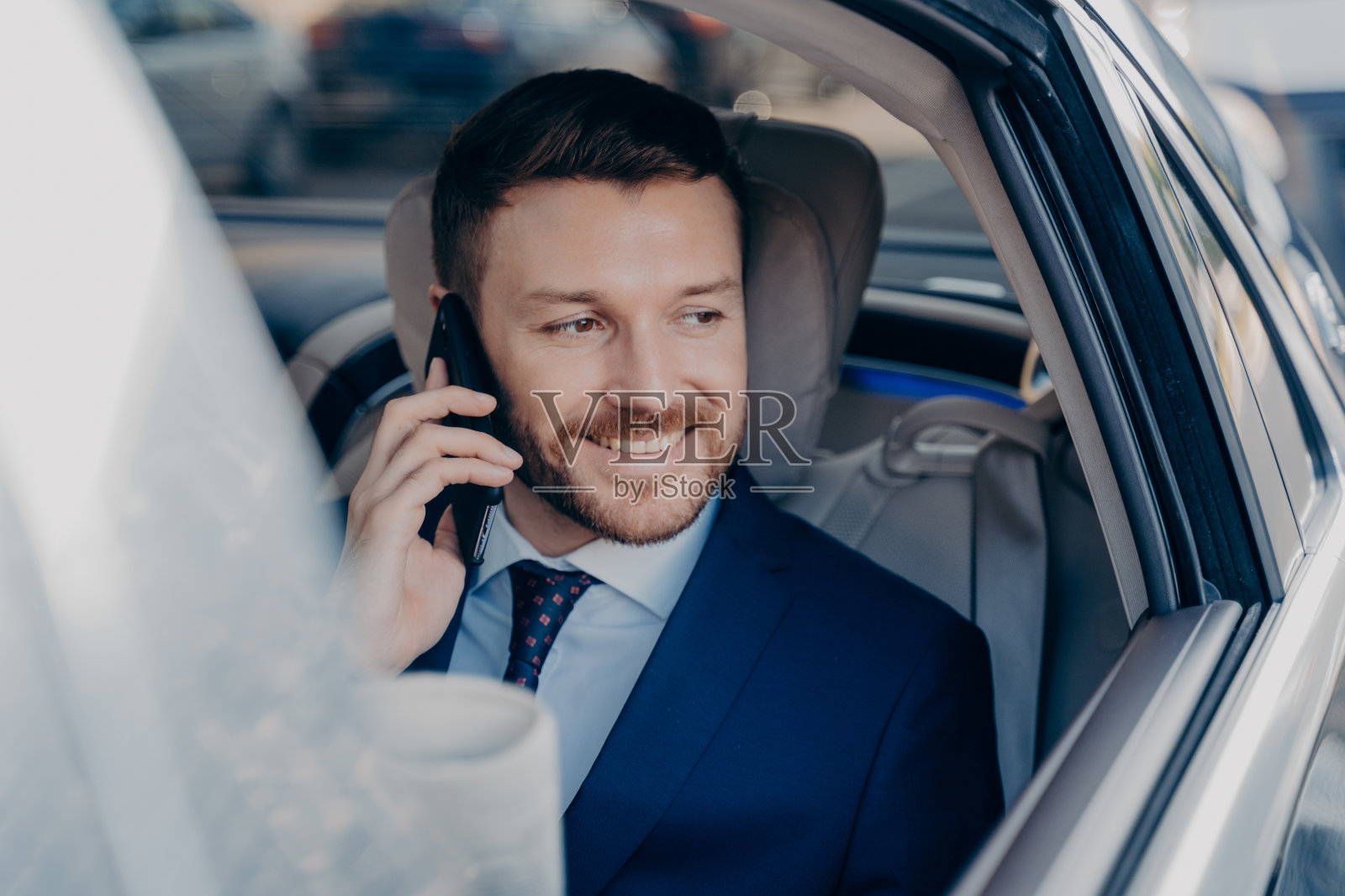 年轻的白人法学家，穿着正式的深蓝色西装，在车里打手机照片摄影图片