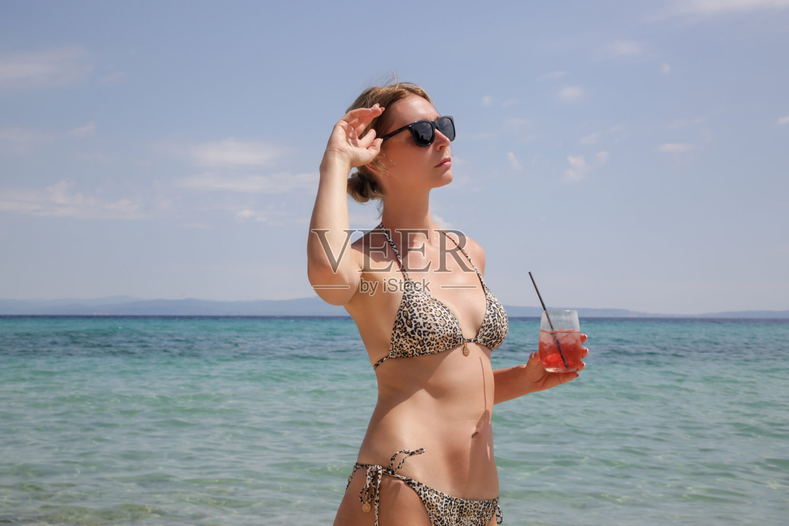 快乐的年轻女子在海滩上喝着粉红色的尼格罗尼鸡尾酒。轻松的热带暑假概念。照片摄影图片