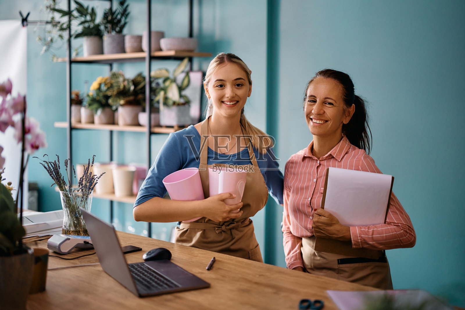 快乐的花店老板和她在花店工作的年轻同事看着相机。照片摄影图片
