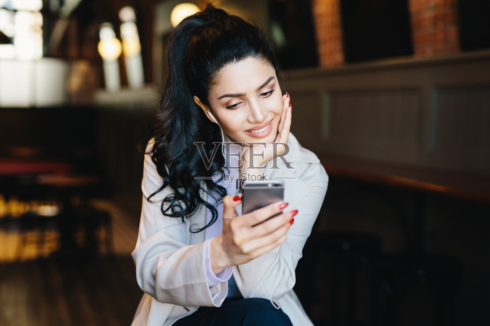 黑色头发，红色指甲，穿着白大褂，看起来很优雅，用手机听歌曲，用电子设备查看电子邮件，和朋友视频通话照片摄影图片