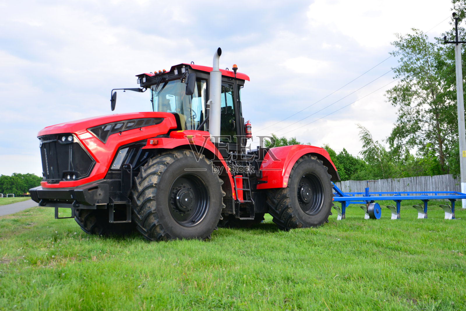 红色的拖拉机在绿色的农田上，背景是多云的天空照片摄影图片