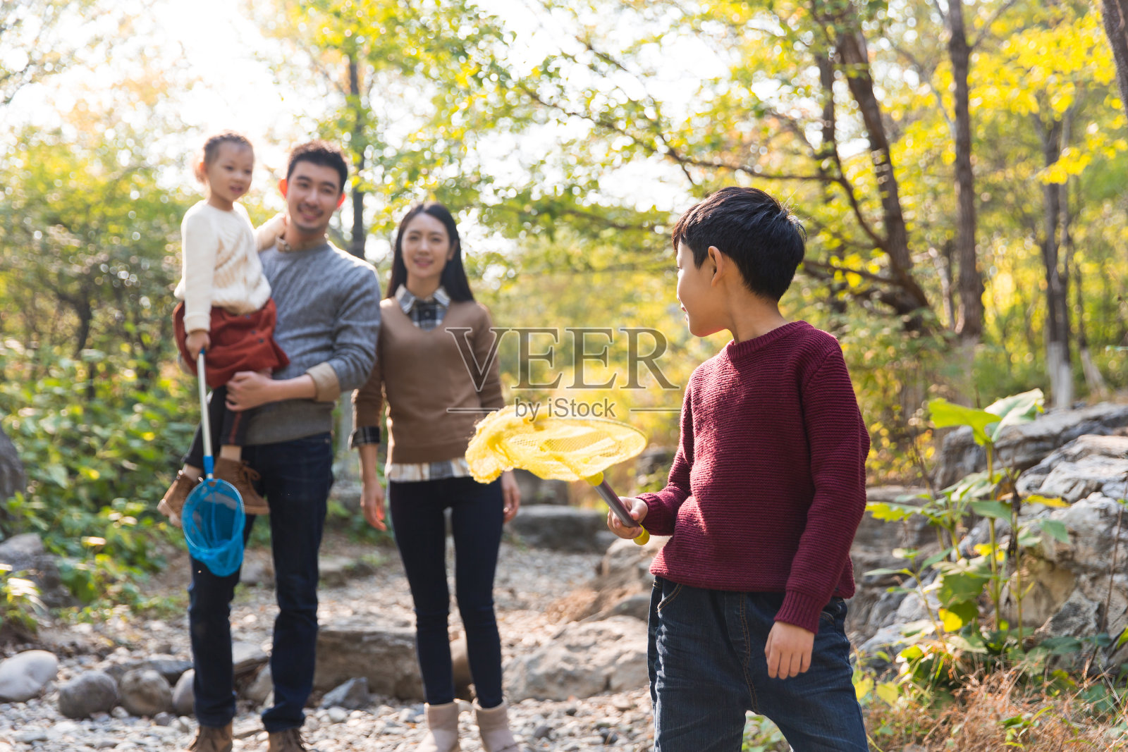 一个年轻的中国四口之家在秋天走在一个森林山涧，小男孩和小女孩与一个昆虫网-库存的照片照片摄影图片