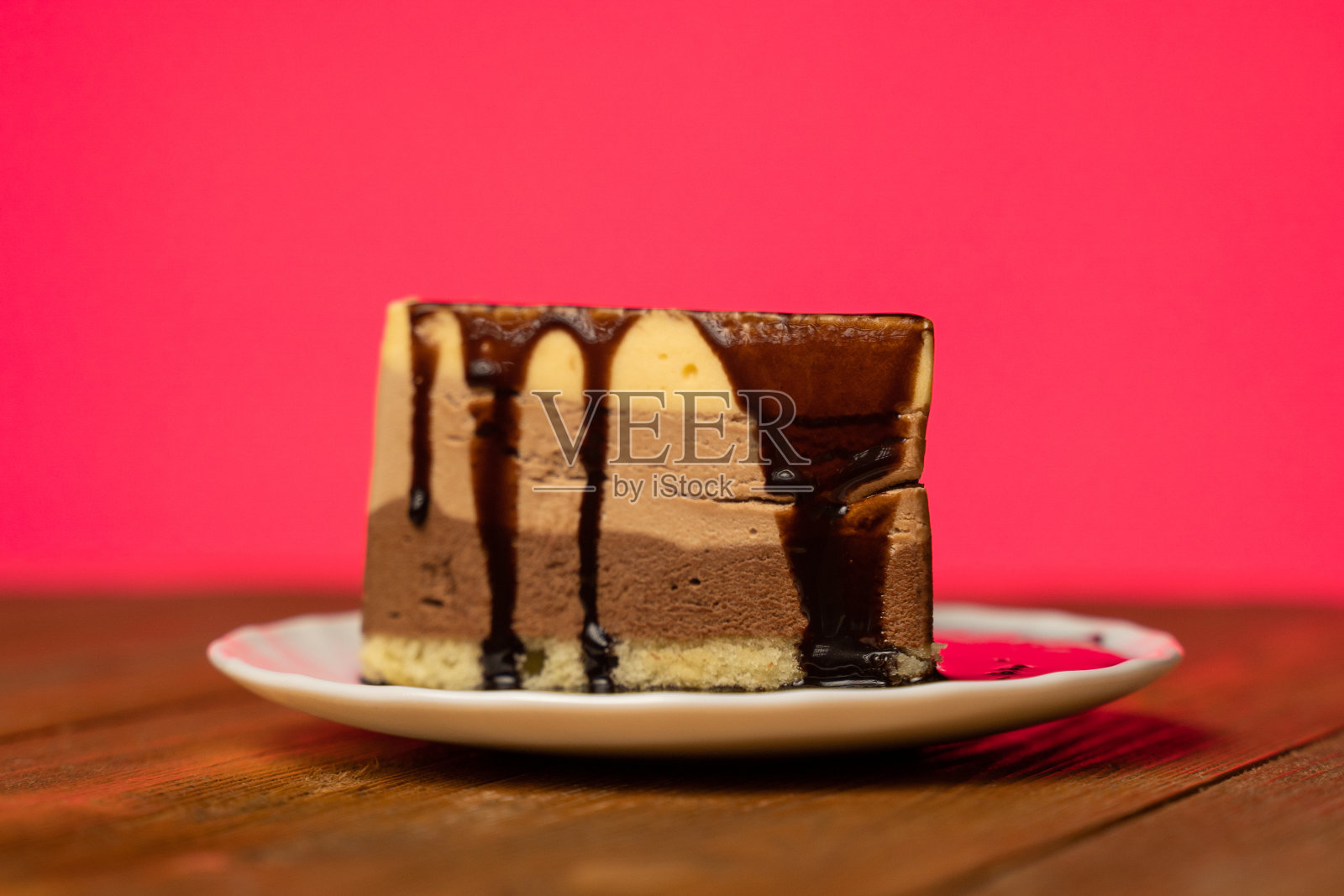 在粉色背景的盘子上，巧克力糖浆浇在巧克力蛋糕上照片摄影图片