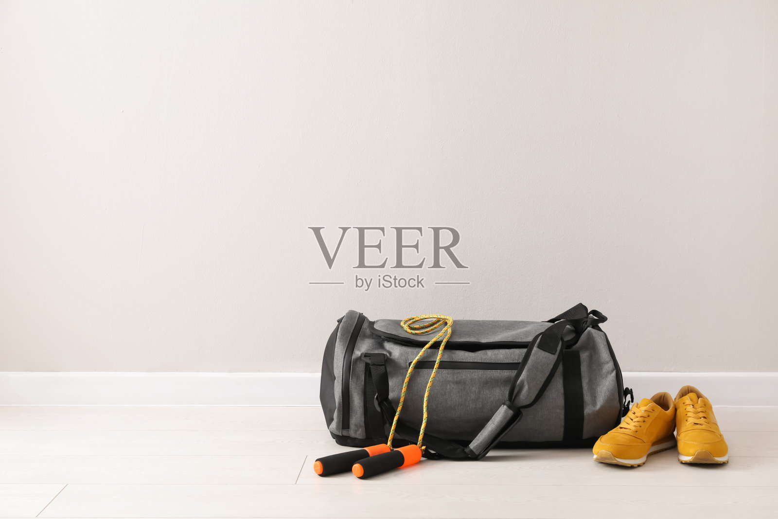 灰色的包和运动配件放在地板上，靠近浅色的墙壁，留出文字空间照片摄影图片