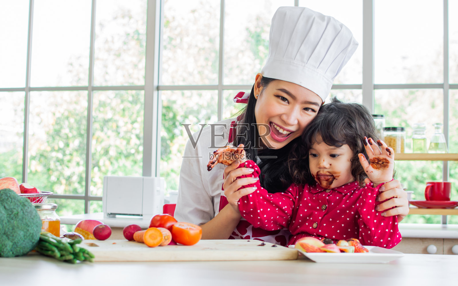 美丽的亚洲妈妈做着美味的巧克力和草莓做早餐，坐在家里舒适的厨房里照顾着她的混血可爱的小女儿，开心地微笑着。照片摄影图片