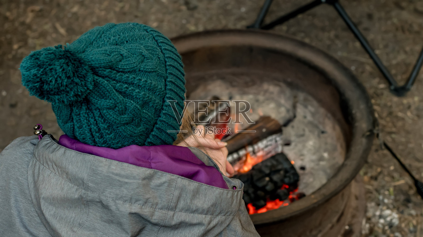 露营生活方式的概念。一个戴着无檐便帽的女孩在露营地的营火上暖手照片摄影图片