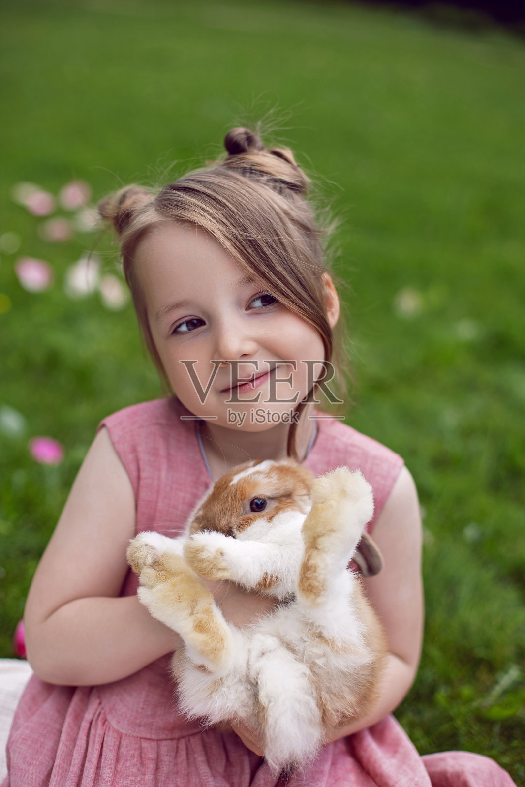 夏天，穿着粉色裙子的小女孩在绿色的草地上和兔子玩耍。复活节期间，孩子和动物之间的有趣友谊照片摄影图片