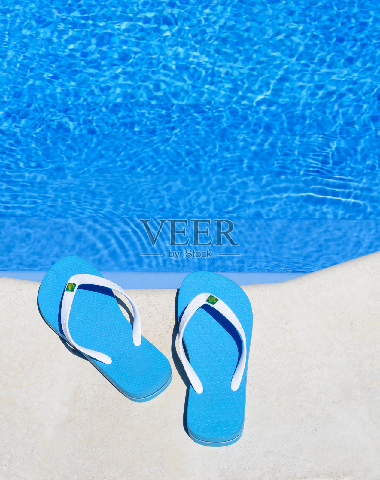 明亮的蓝色人字拖放在水池的背景上。照片摄影图片