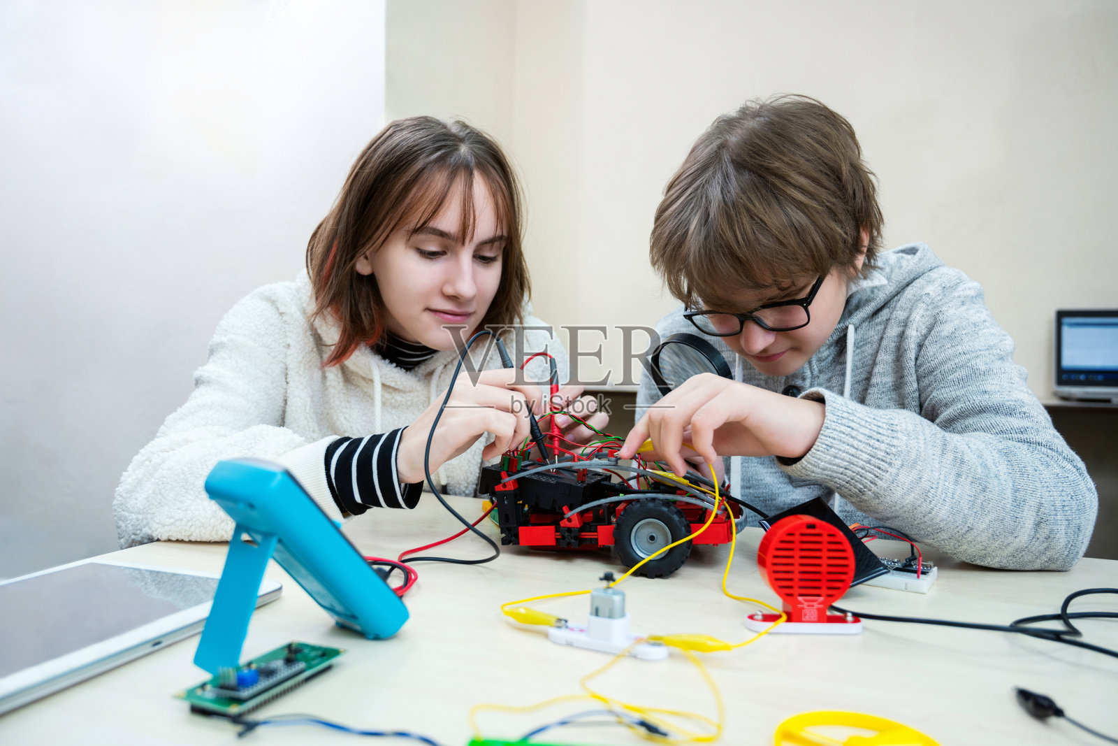 制作机器人汽车的学生。十几岁的女孩和男孩在机器人学校从建筑工管制机器人，孩子学习机器人建造。照片摄影图片