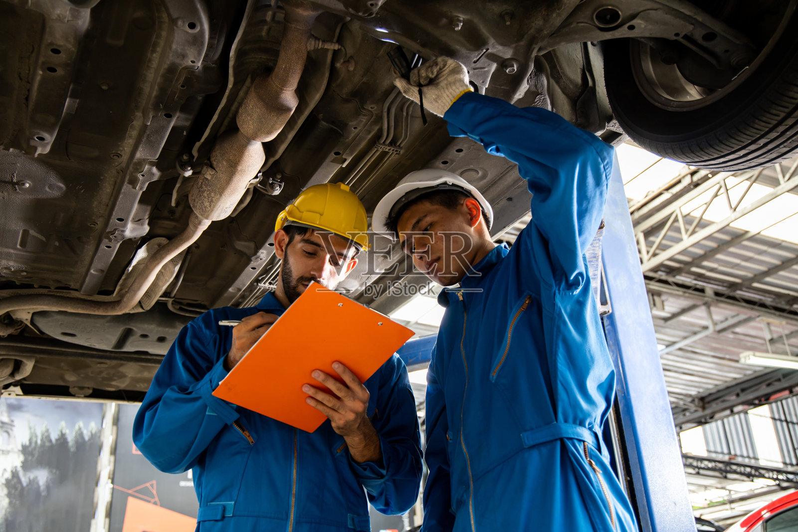 两个机械师正在检查汽车的悬挂系统。照片摄影图片