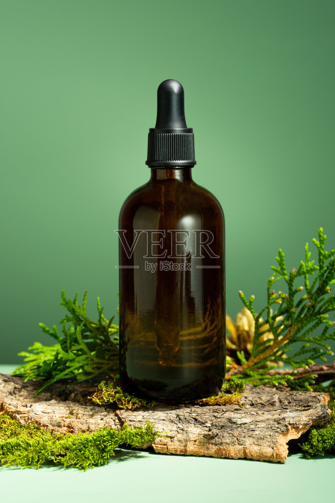 玻璃瓶身体油。绿色背景上的精油、苔藓和树皮的概念组合。用于皮肤和头发护理的油脂精华液。自我照顾与健康，森林与自然主题照片摄影图片