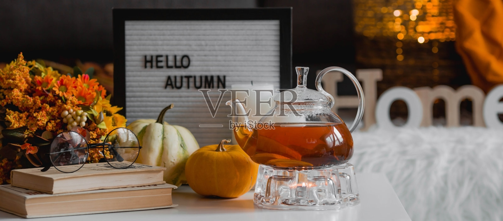 舒适的秋天的概念。寒冷天气里的家庭温暖。静物。客厅里的咖啡桌上放着一条毯子、南瓜、一个茶壶和一杯茶。照片摄影图片