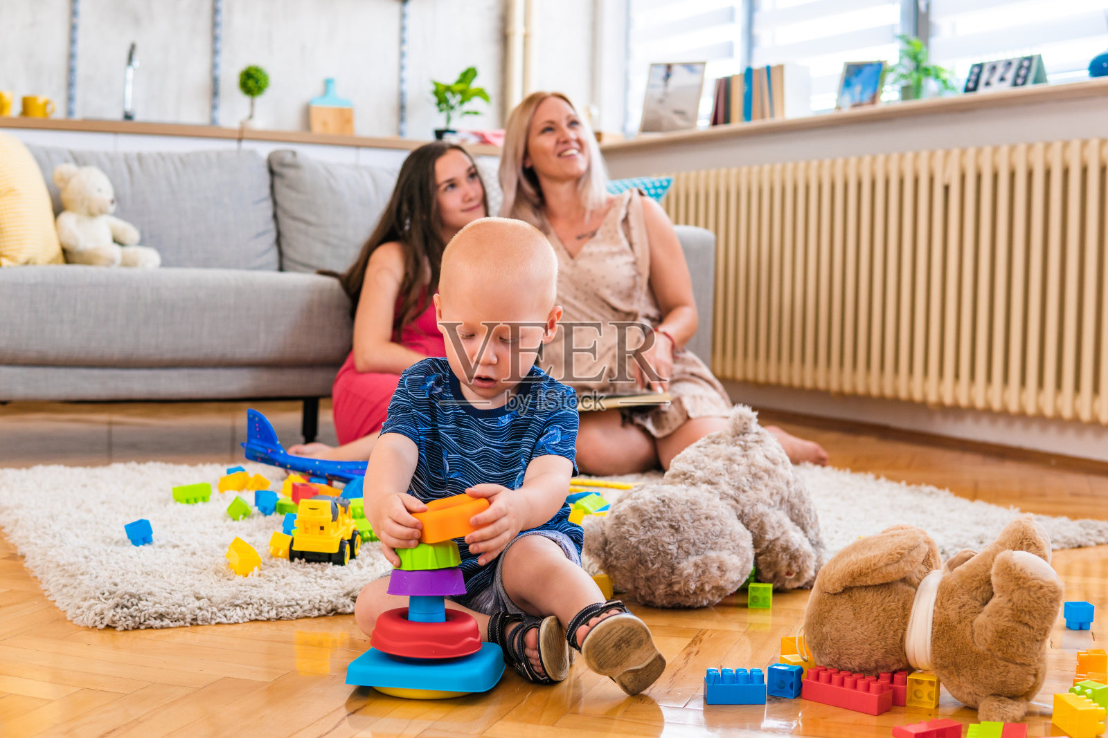 一个小男孩在家里的地板上玩耍，被一个幸福的家庭包围着。照片摄影图片