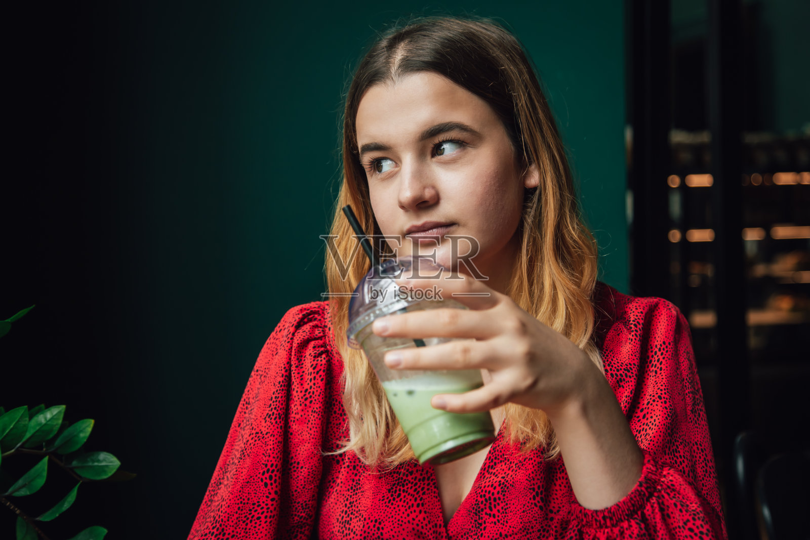 一个年轻的女人在咖啡馆喝一杯绿色饮料冰拿铁。照片摄影图片