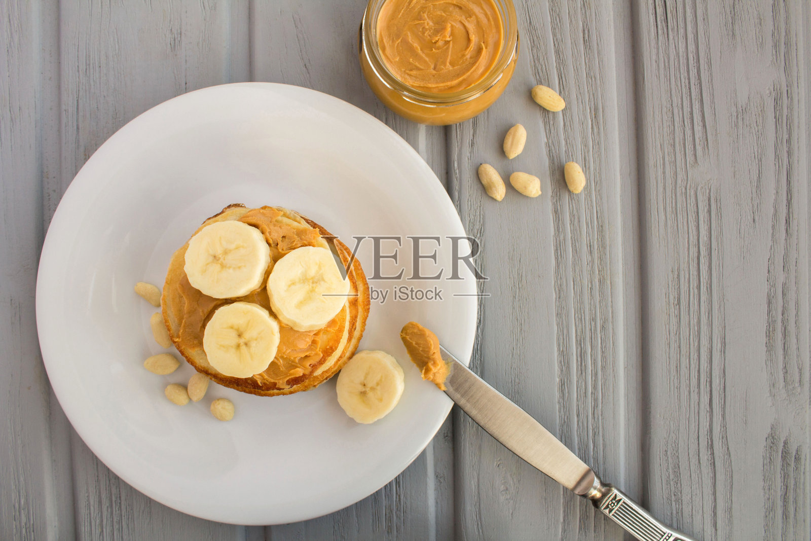 在灰色的木制背景上，白色的盘子里放着花生酱和香蕉的自制煎饼。前视图。副本的空间。照片摄影图片