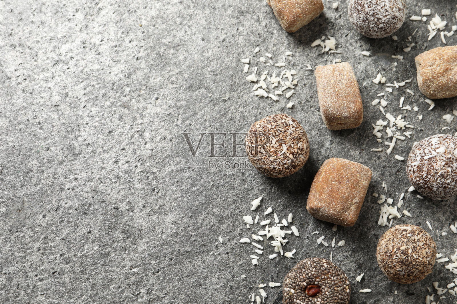 不同美味的素食糖果球和干燥的椰子放在灰色的桌子上，平铺着。空间的文本照片摄影图片