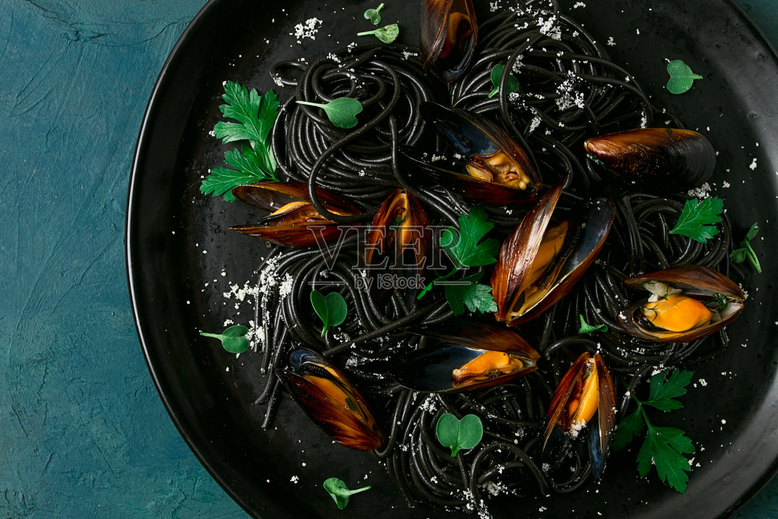 黑鱿鱼意大利面，黑意大利面，煮贻贝，放在黑色盘子里，配上欧芹和帕尔马干酪，特写，选择性聚焦，没有人，照片摄影图片