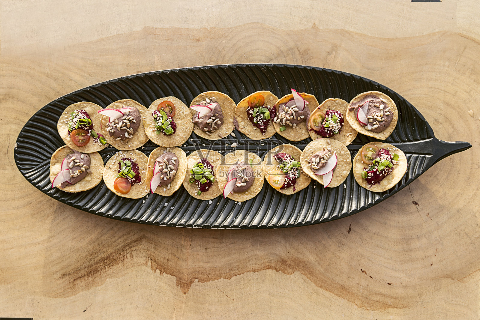 素食餐前小吃，盛在一个黑色的叶子形状的盘子里照片摄影图片