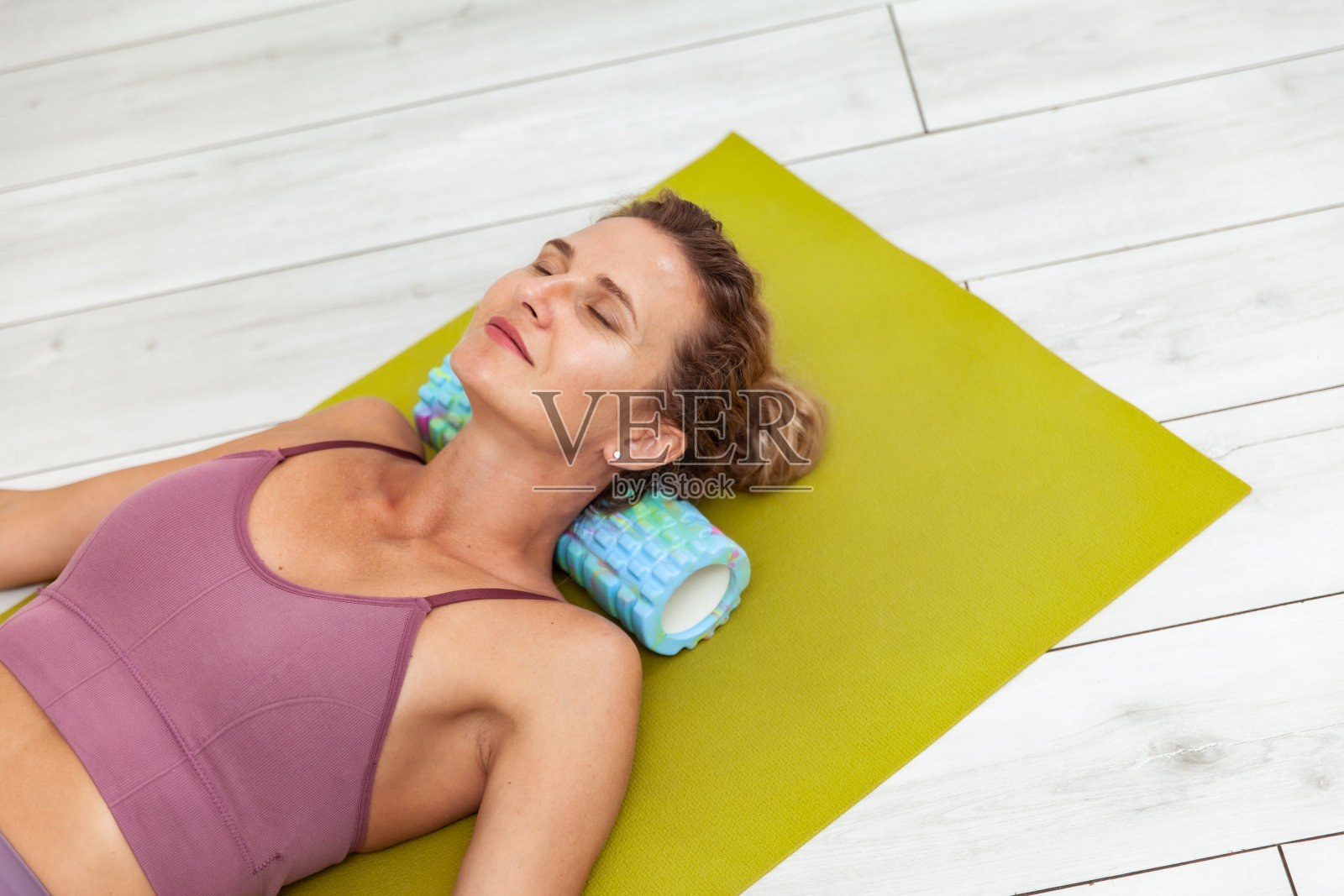 年轻女子躺在垫子上用按摩辊按摩颈部肌肉，放松颈部肌肉照片摄影图片