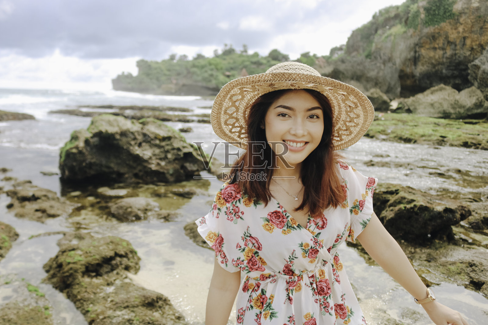 在印尼Gunungkidul，一个年轻的亚洲女孩戴着沙滩帽在蓝天沙滩上休息照片摄影图片