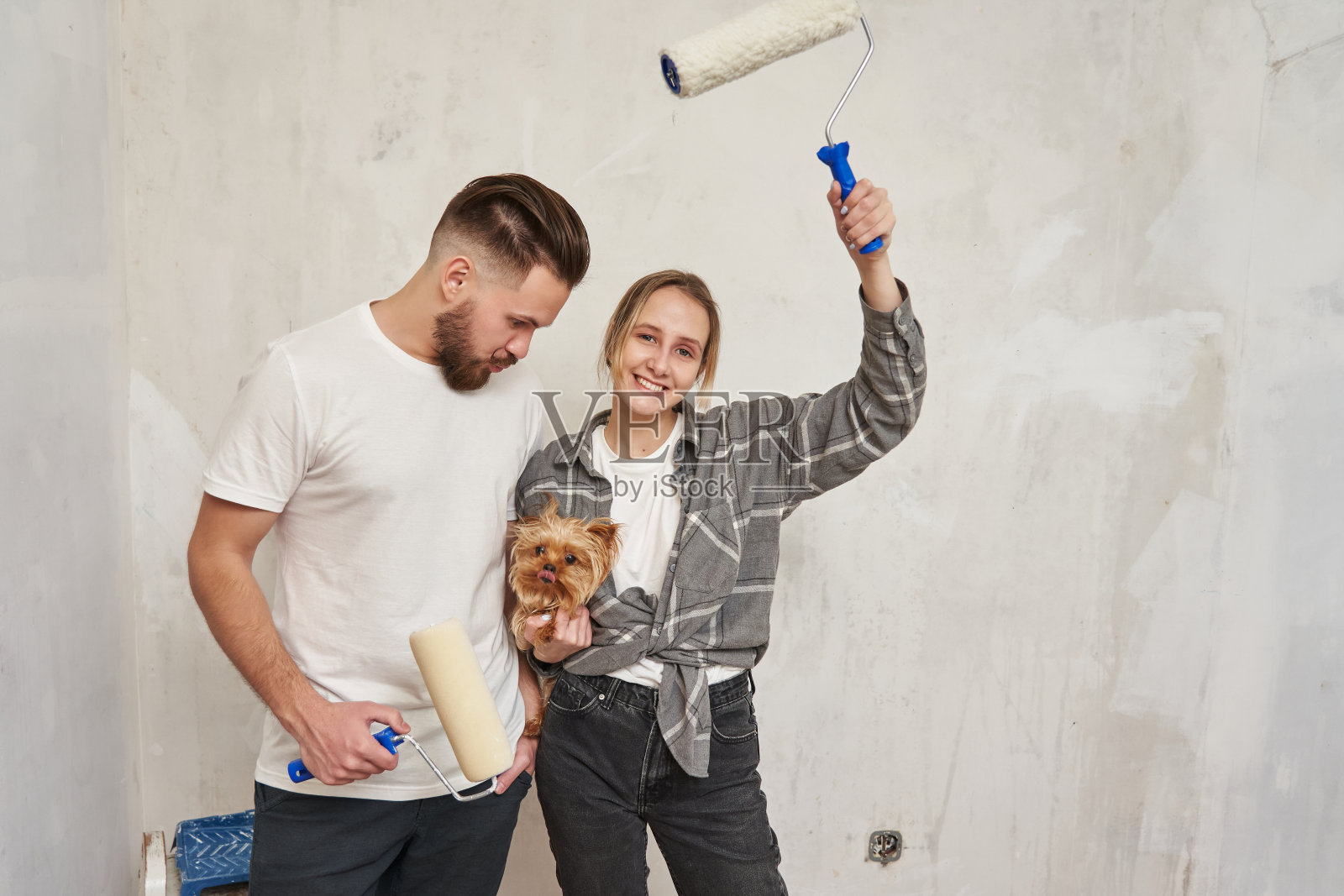 年轻的家庭，小狗和油漆辊。一个年轻的家庭和一个愉快的改造的概念。第一个家，公寓装修照片摄影图片