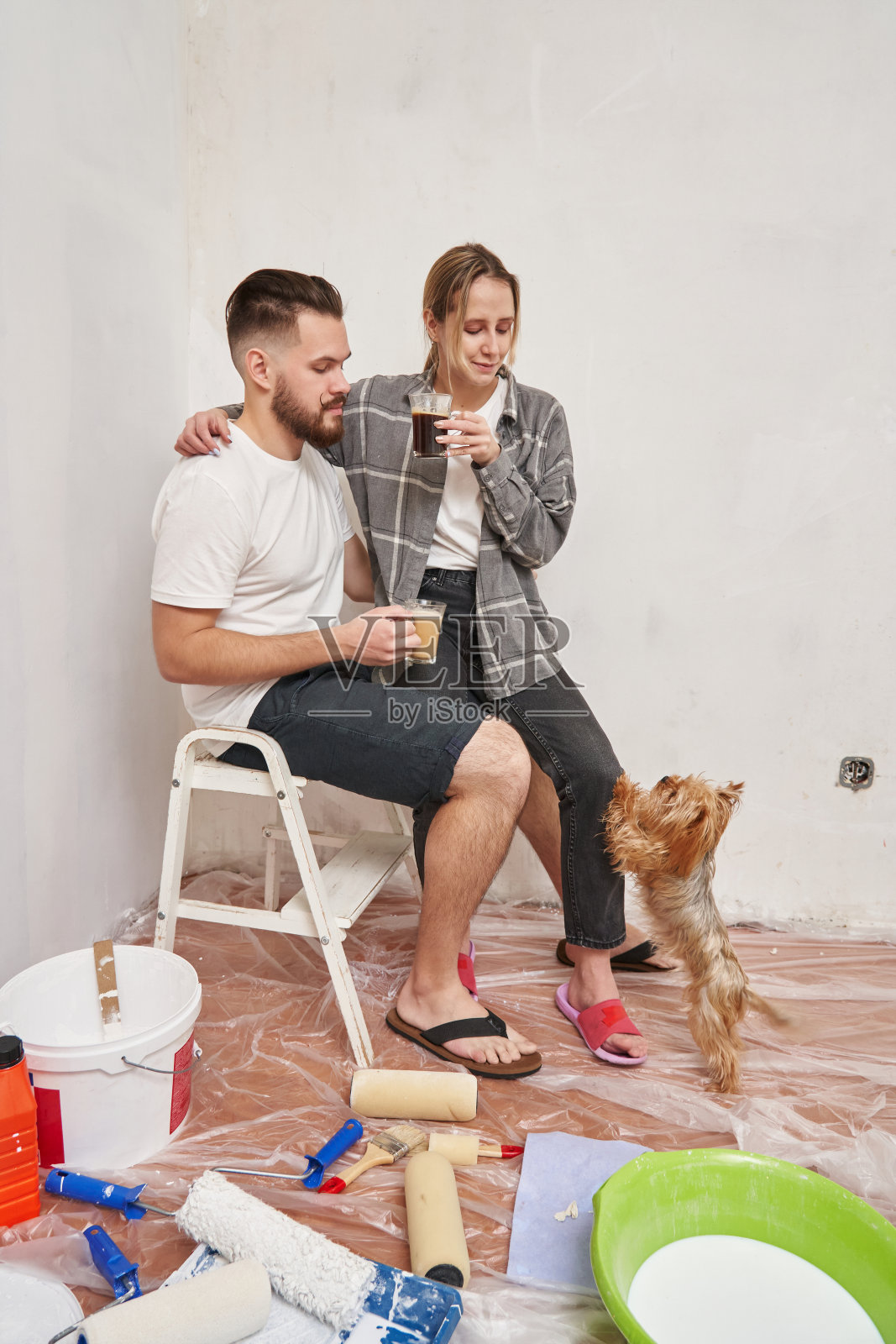 一对年轻夫妇在公寓维修的背景下。坐在梯子上，前面是建筑用品和一只小狗。壁画概念照片摄影图片