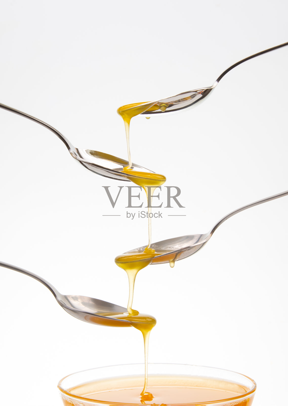 在白色的背景上，新鲜的花朵蜂蜜从一个勺子滴到另一个勺子。有机维生素的食物。照片摄影图片