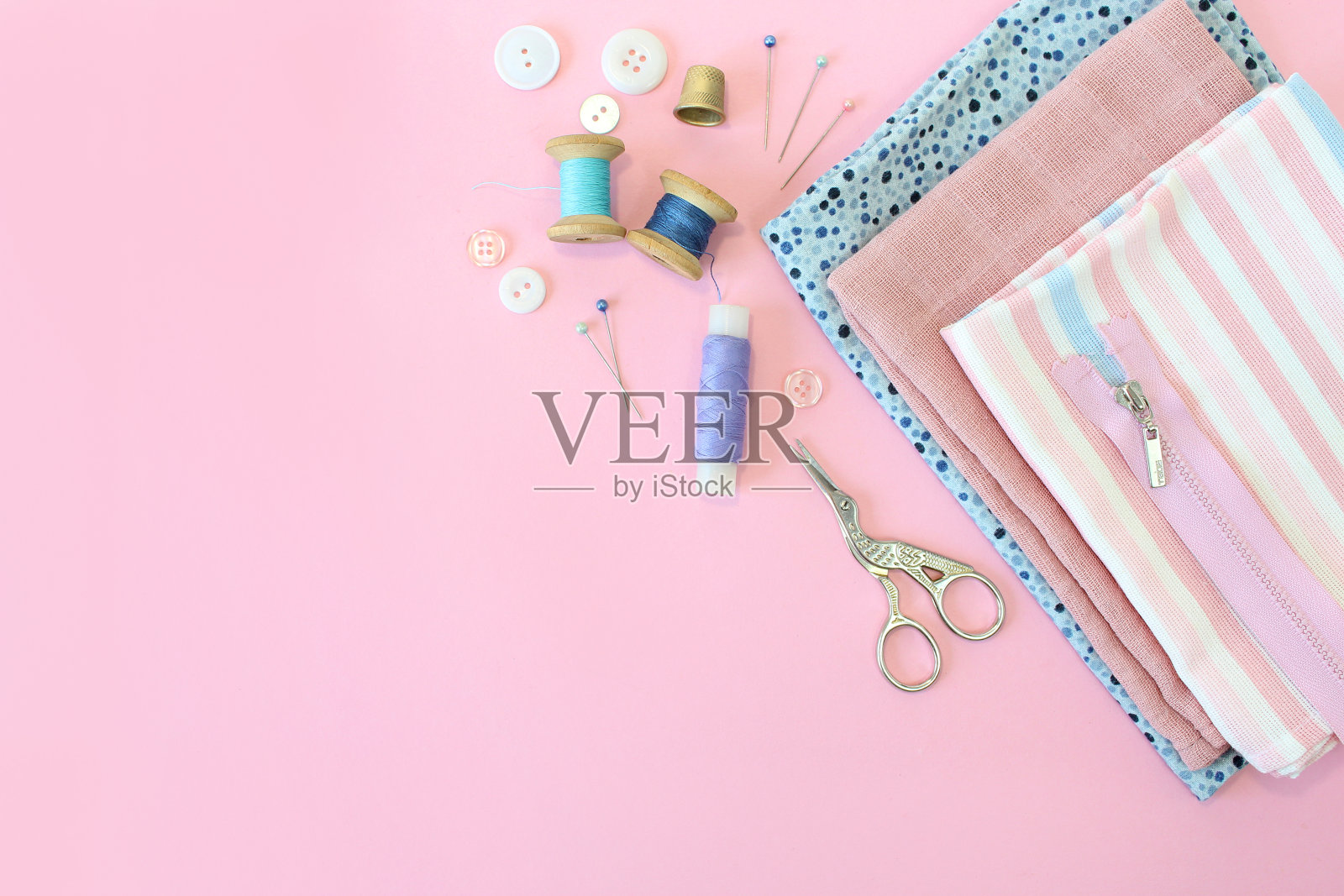 缝纫配件和织物在粉红色的背景。缝纫线，针，别针，织物，纽扣和缝纫厘米。顶视图,flatlay照片摄影图片