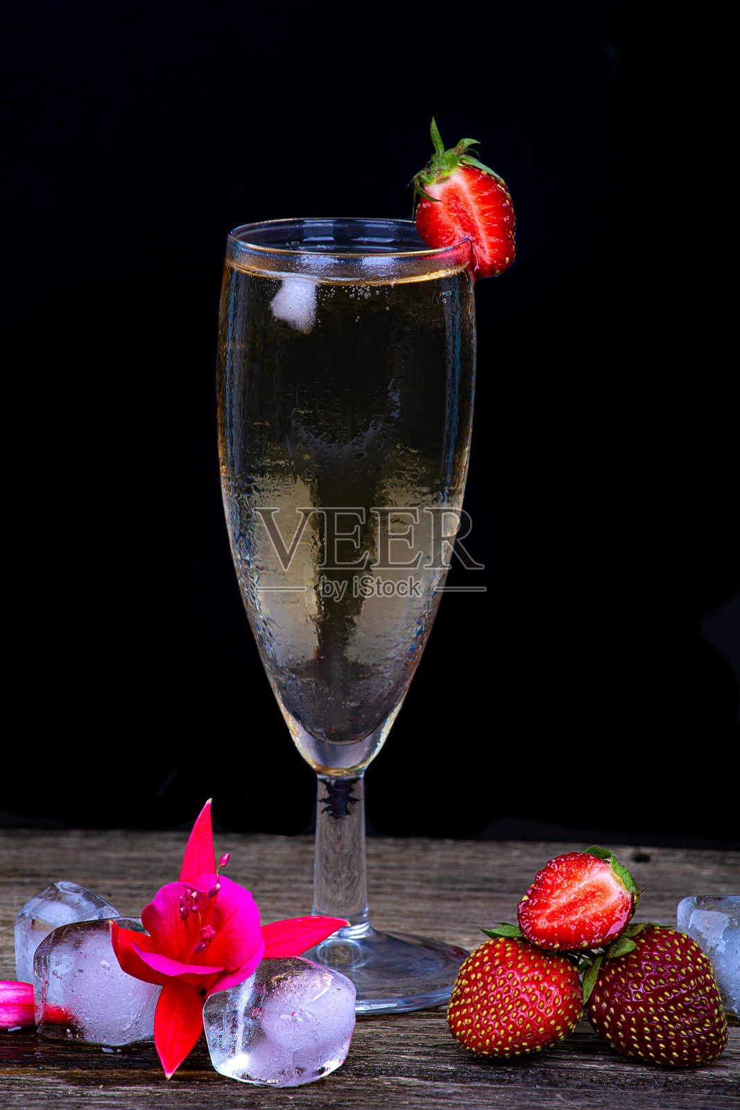 在黑色的背景上，一杯雾气弥漫的香槟、新鲜的草莓和冰块照片摄影图片