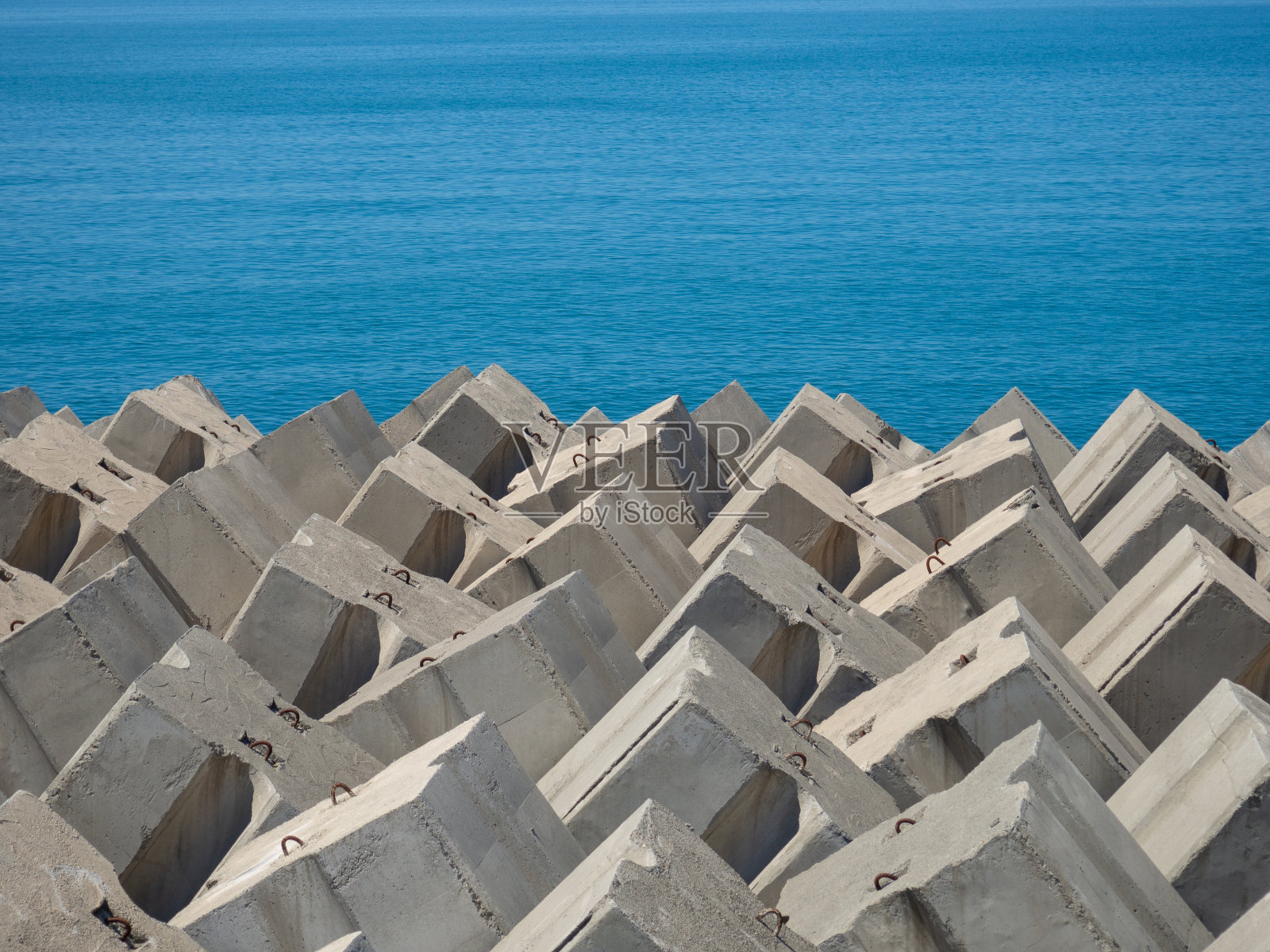 岸边有混凝土防波堤和成堆的石头。石头拍打着海浪。海岸保护。照片摄影图片