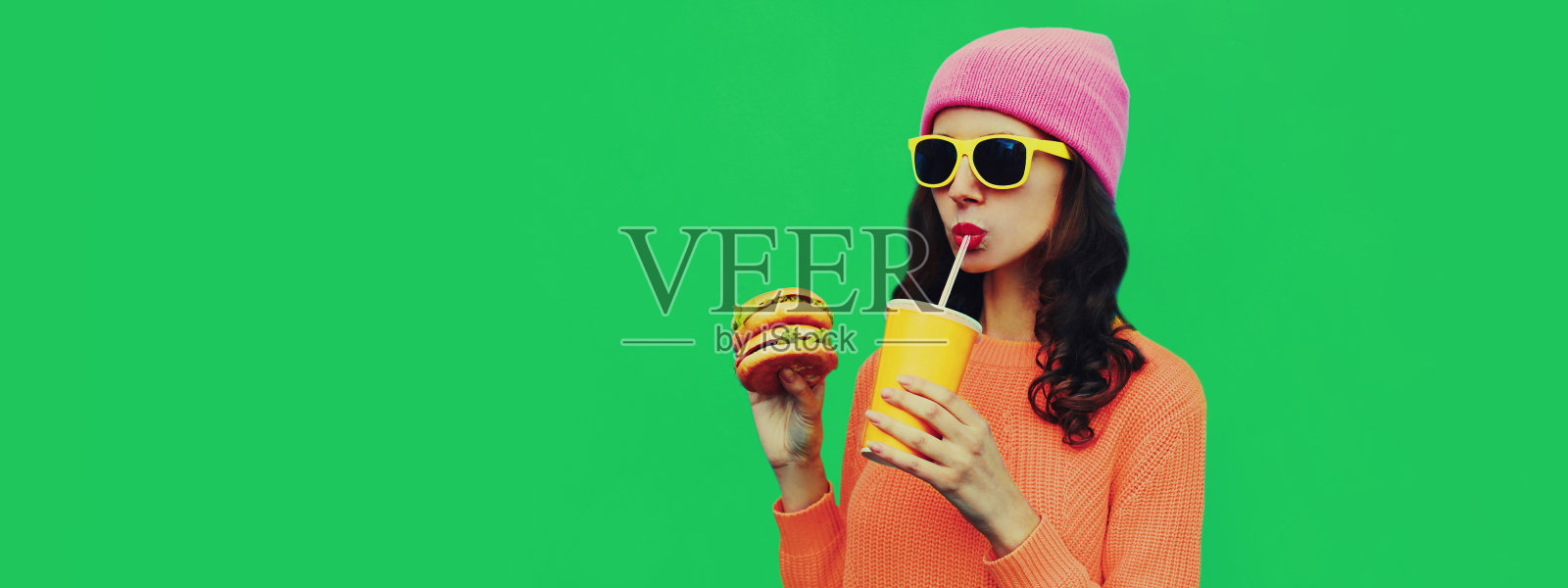 时髦的年轻女子喝果汁与汉堡快餐的肖像在绿色的彩色背景照片摄影图片
