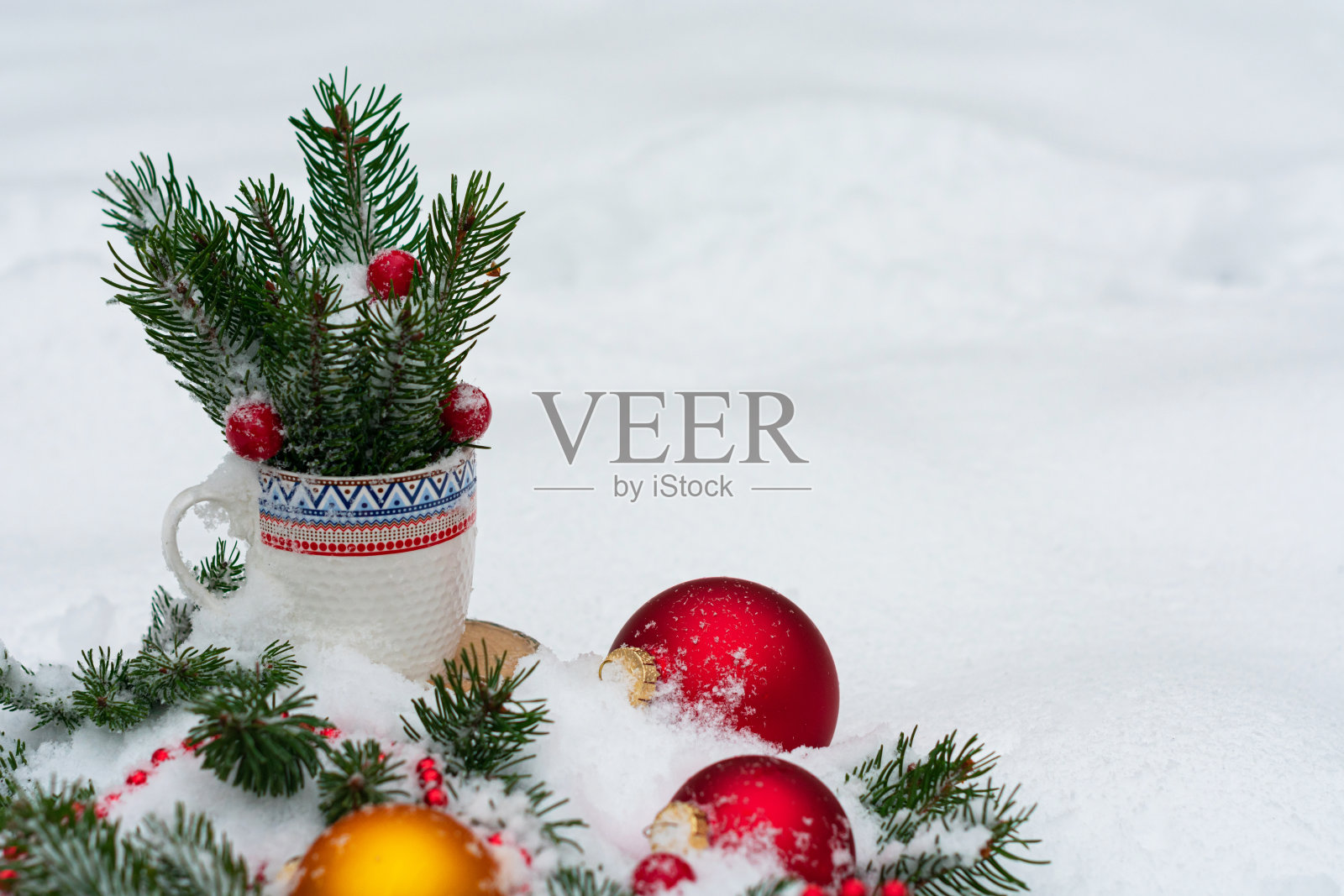 针叶树的树枝上装饰着圣诞树的玩具，躺在雪地上，放在一个边缘有彩色图案的白色杯子里。在框架的右边有一个文本的地方照片摄影图片