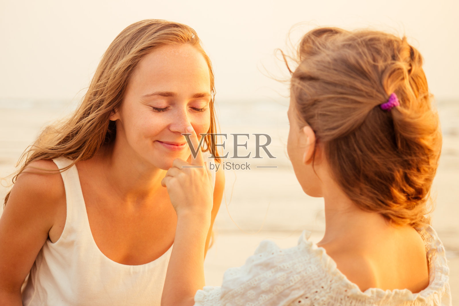 母亲和十几岁的女儿在海滩上使用防晒霜照片摄影图片