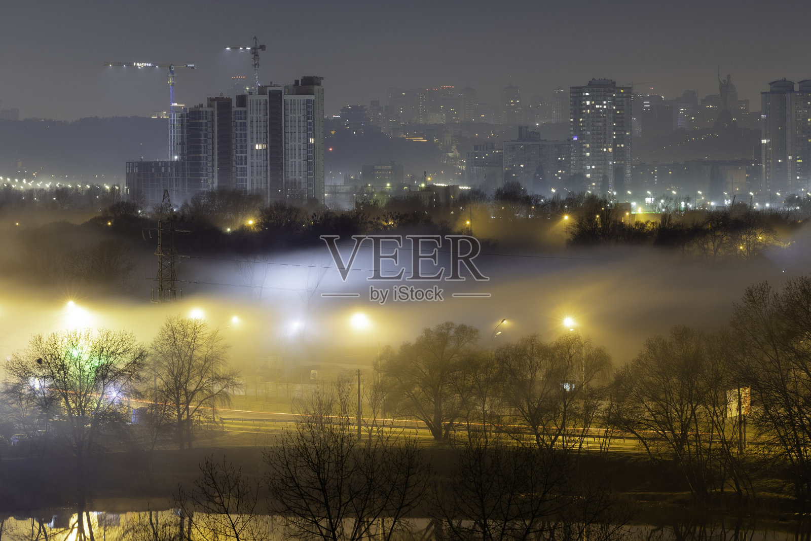 大城市的夜景。令人敬畏的明亮，多色的光在浓雾中空旷的街道上。卧室社区的公寓大楼，通勤城镇地区。Darnytsia,基辅。2021年乌克兰。照片摄影图片