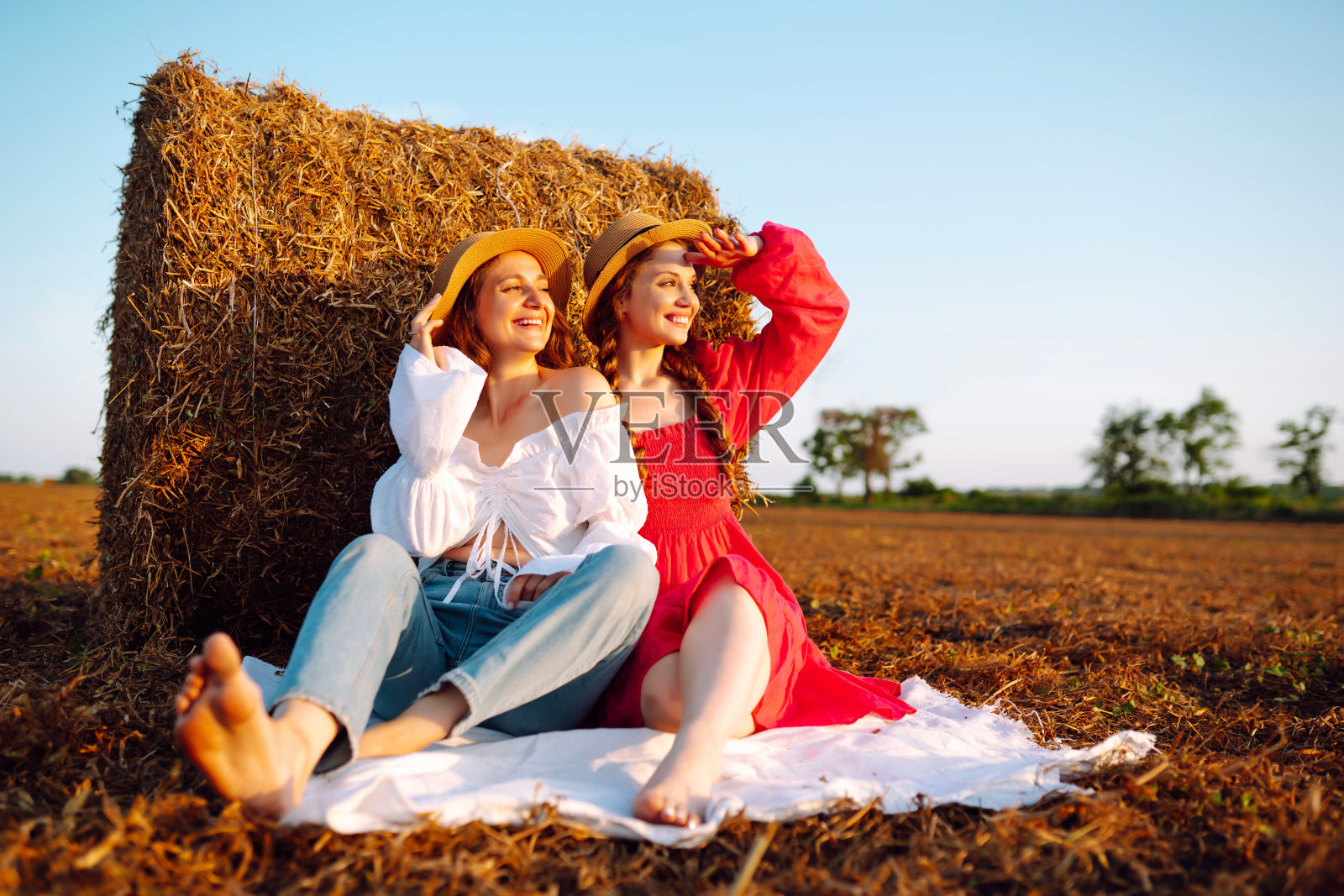 日落时分，两个年轻女子在干草堆旁。照片摄影图片