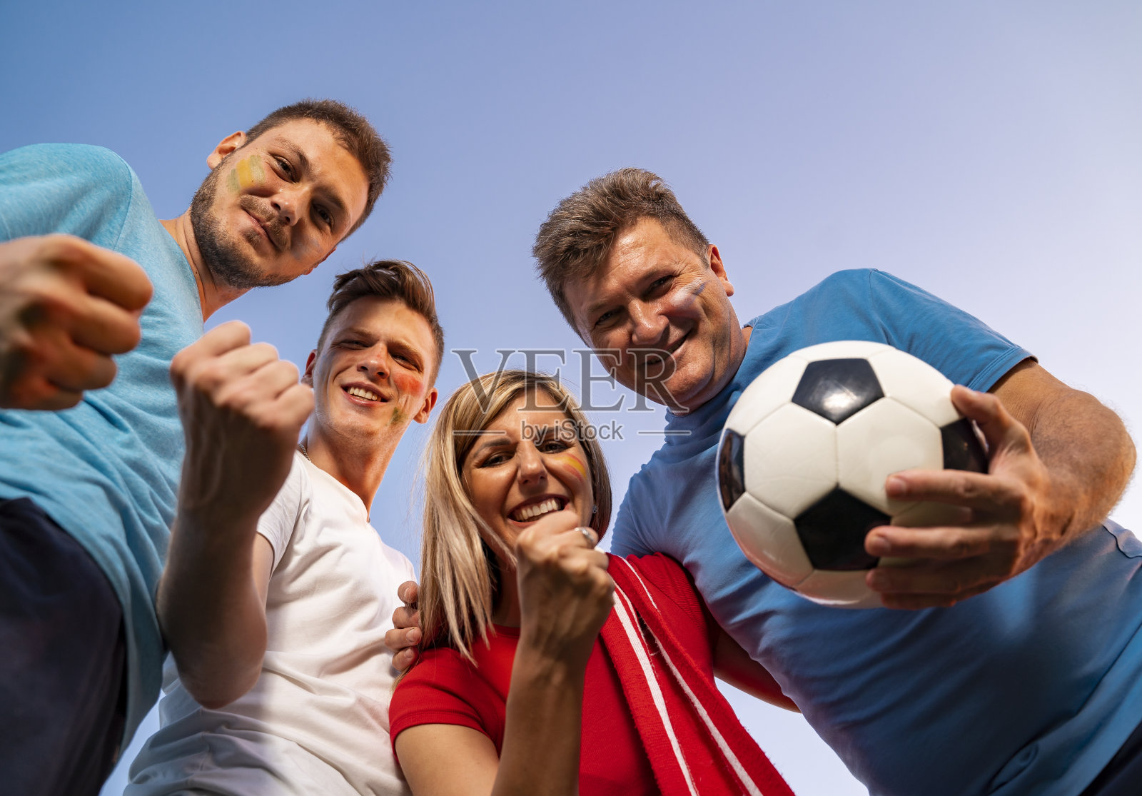 一群欣喜若狂的粉丝拥抱在一起，从下面看，天空背景。脸上涂上油漆，开启有趣模式!照片摄影图片