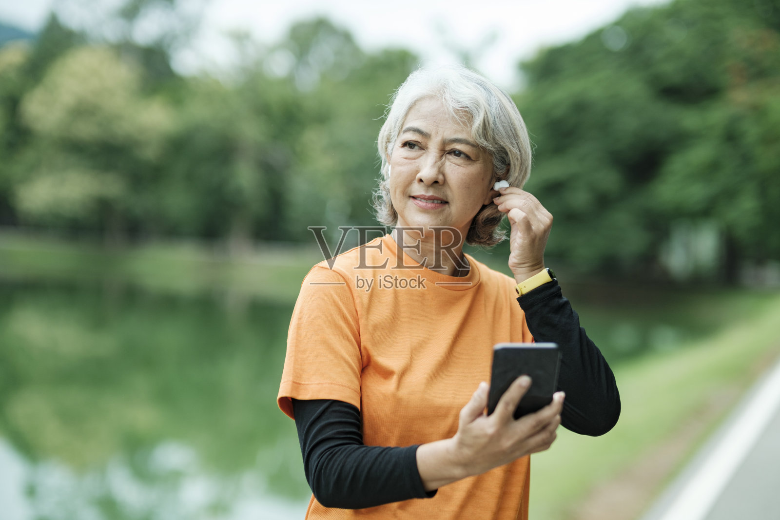 快乐的运动年长妇女听音乐的手机和检查她的智能手表在公园照片摄影图片