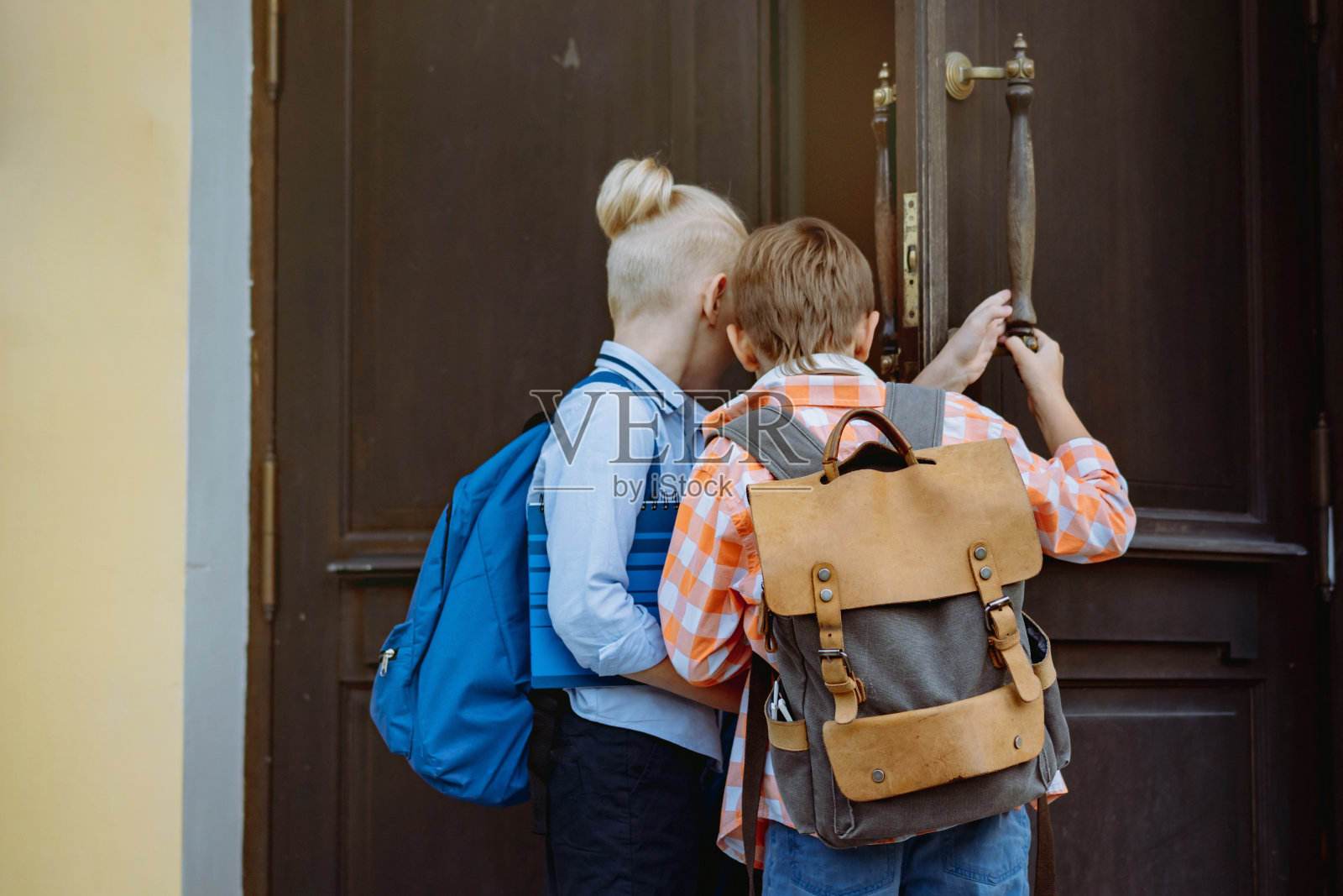 孩子们进入学校打开大木门。阳光明媚的日子，孩子们背着书包站在学校门口。学年开始。照片摄影图片
