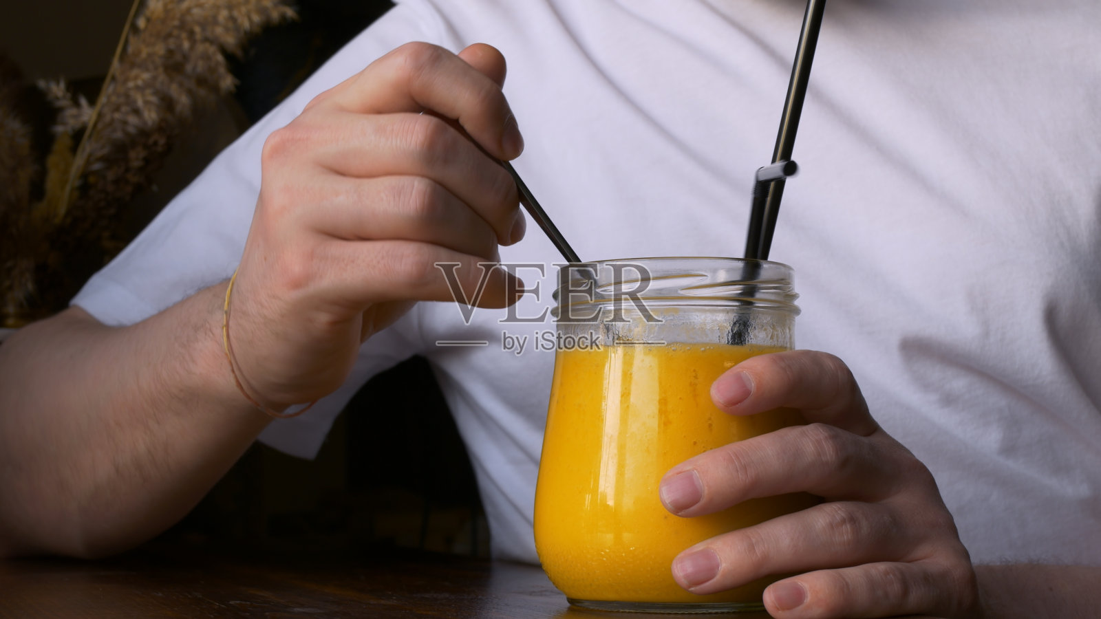 特写的一个男人吃黄色芒果奶昔从一个小勺子的玻璃杯子。咖啡里美味的芒果奶昔，成熟香甜如蜜。食用水果冰沙。照片摄影图片