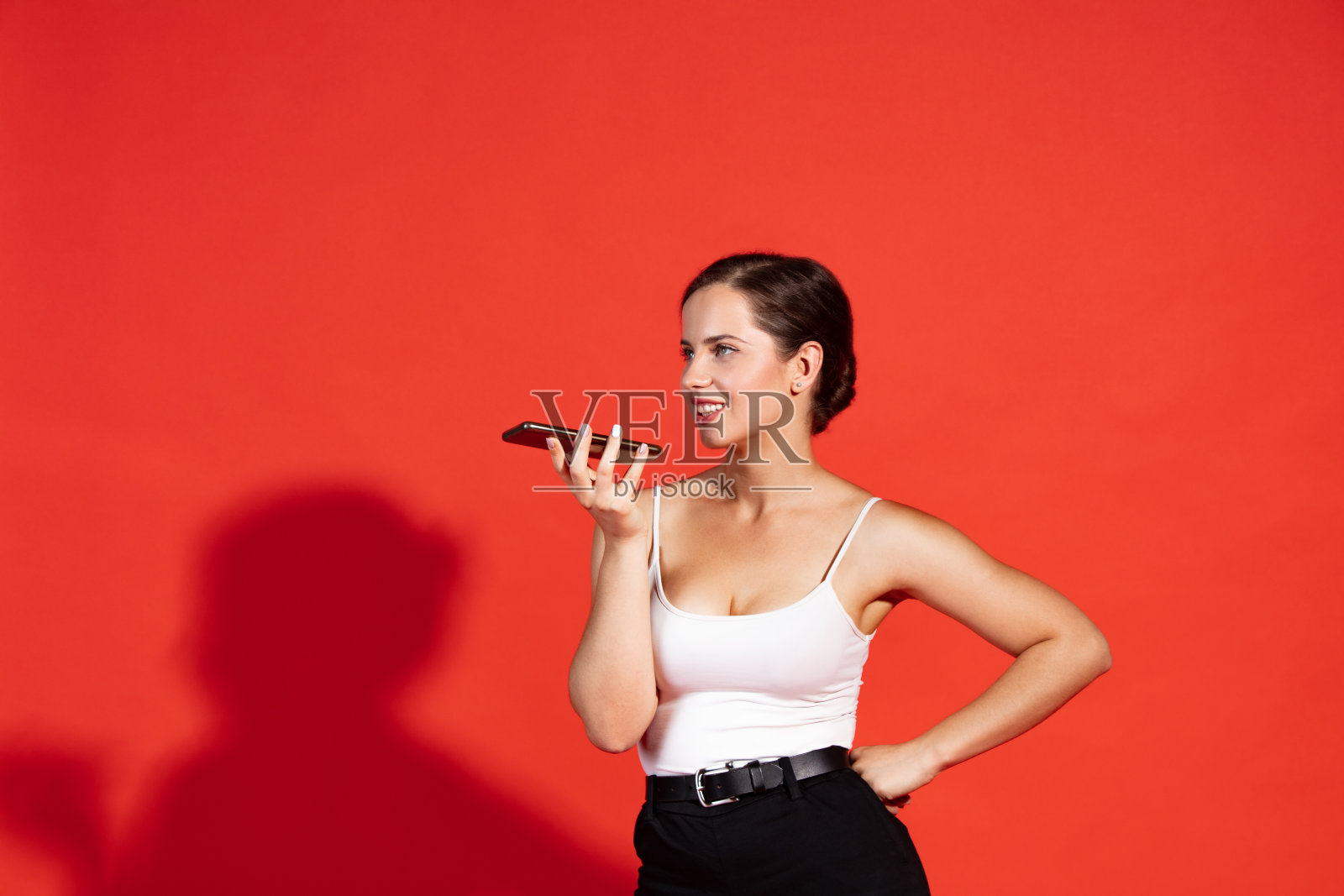 肖像美丽的年轻女子在休闲服装录音语音信息孤立在红色演播室背景。在线交流照片摄影图片