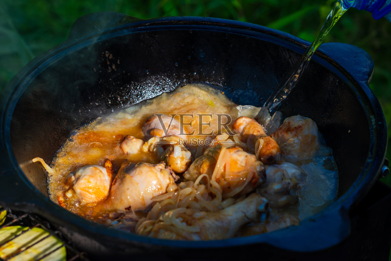 新鲜多汁的鸡腿和洋葱一起在铸铁大锅里用植物油炸。在鸡肉中加水炖煮。格鲁吉亚chakhokhbili配鸡肉。小景深。食物在自然界中照片摄影图片