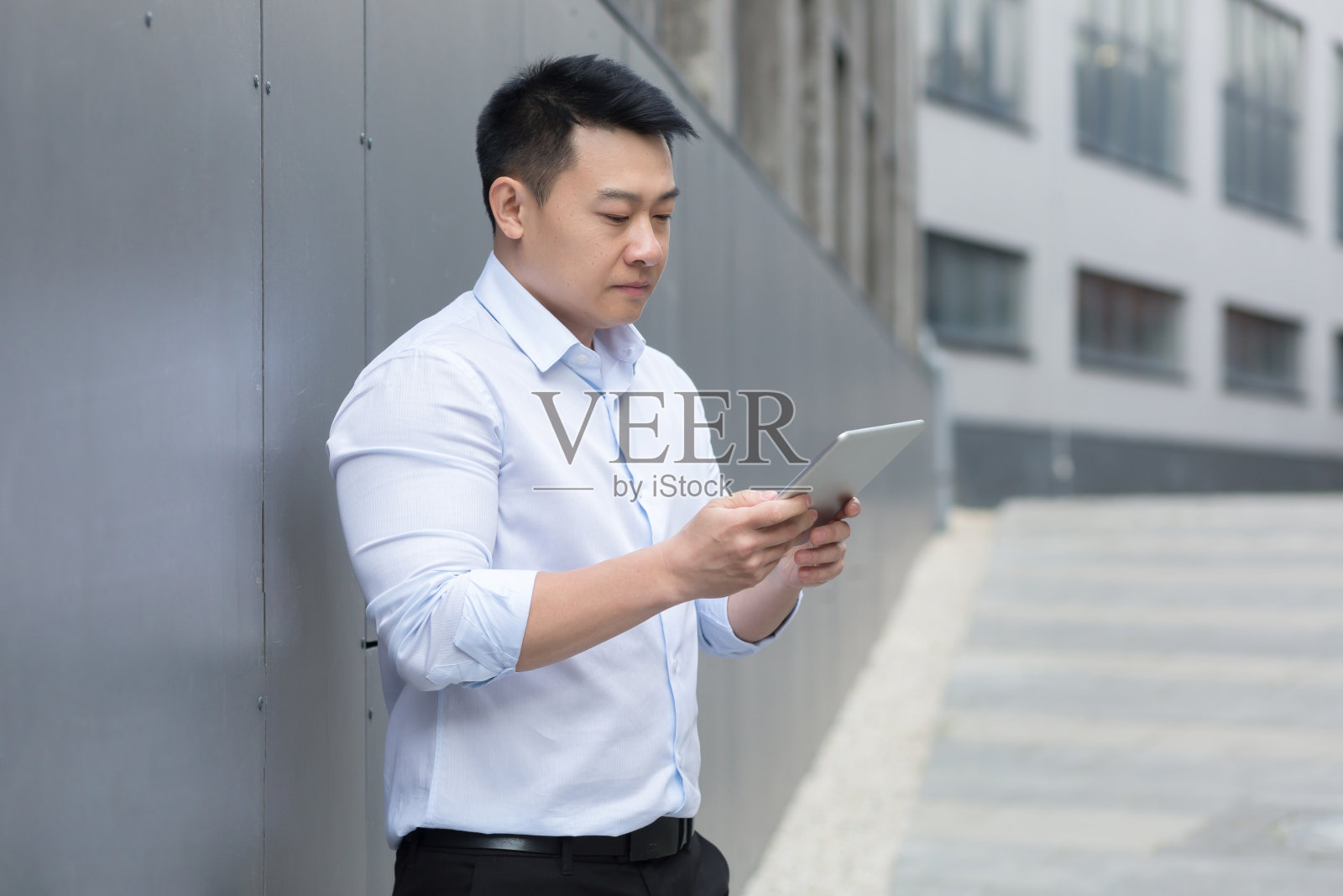 思考亚洲商人在办公大楼外用平板电脑阅读新闻照片摄影图片