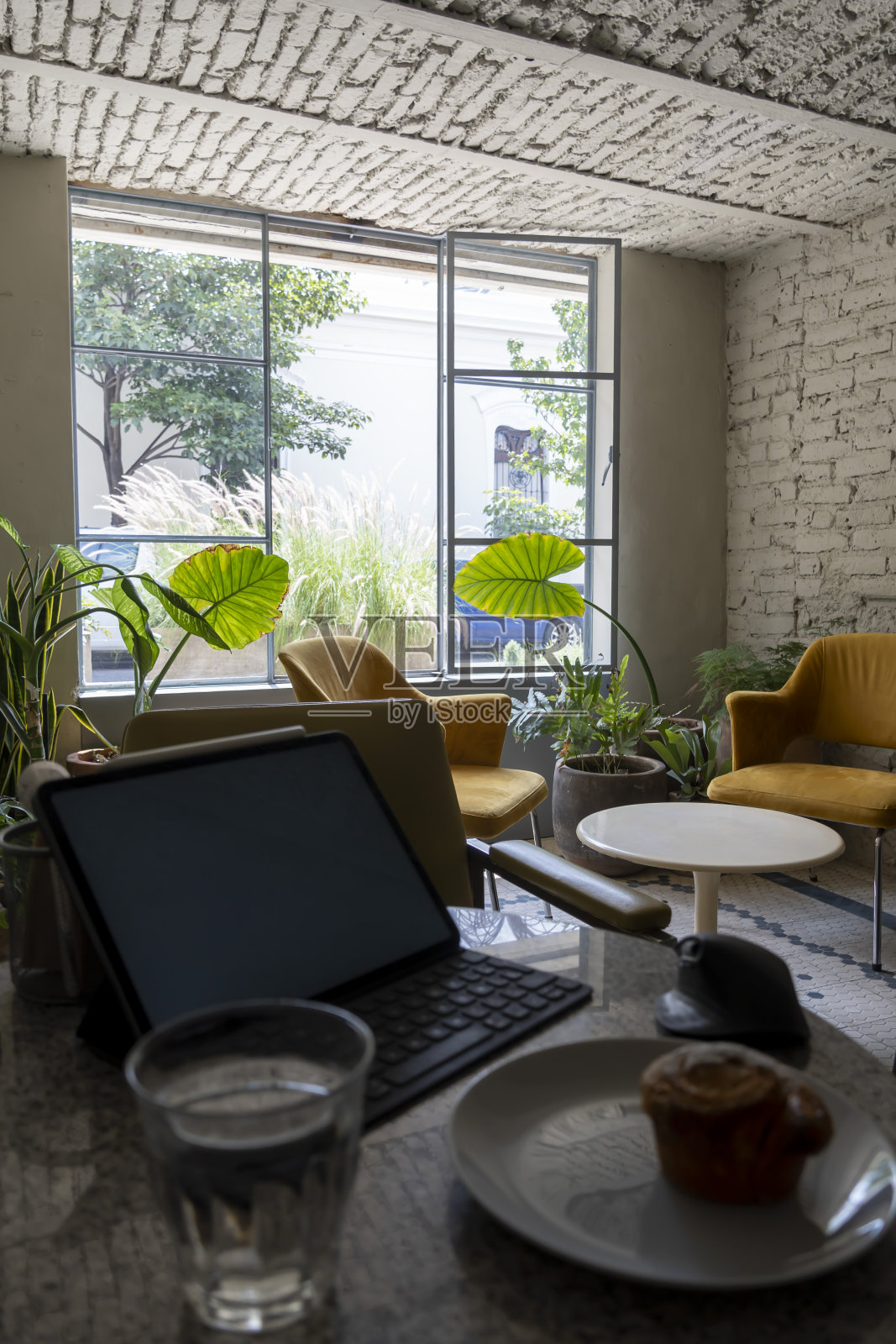 烧饼或纸杯蛋糕放在陶瓷盘子上，平板放在后面。一边工作，一边在两把扶手椅后面享用甜面包照片摄影图片