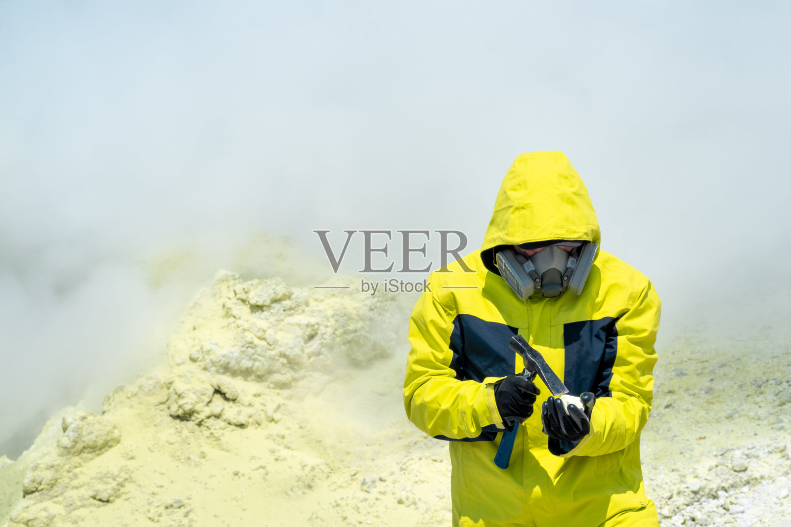 男火山学家在火山斜坡上，在火山喷口的蒸汽中检查一种矿物样本照片摄影图片