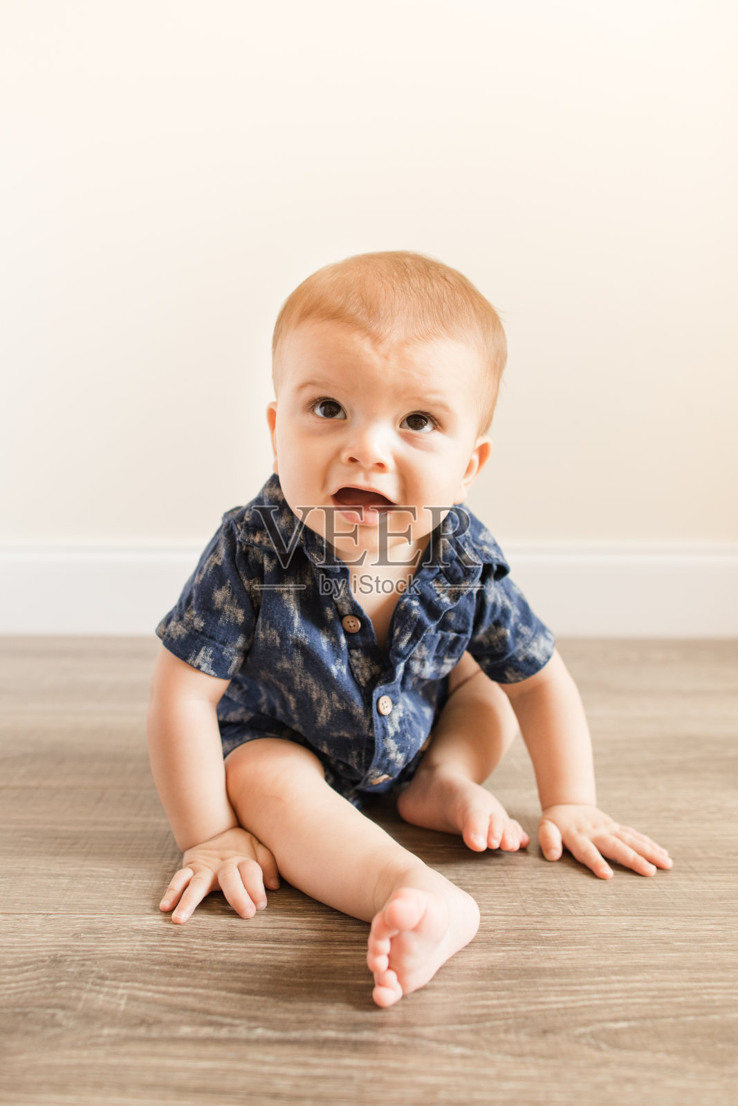7个月大的小男孩穿着蓝色亚麻系扣连体裤独自坐在木地板上照片摄影图片