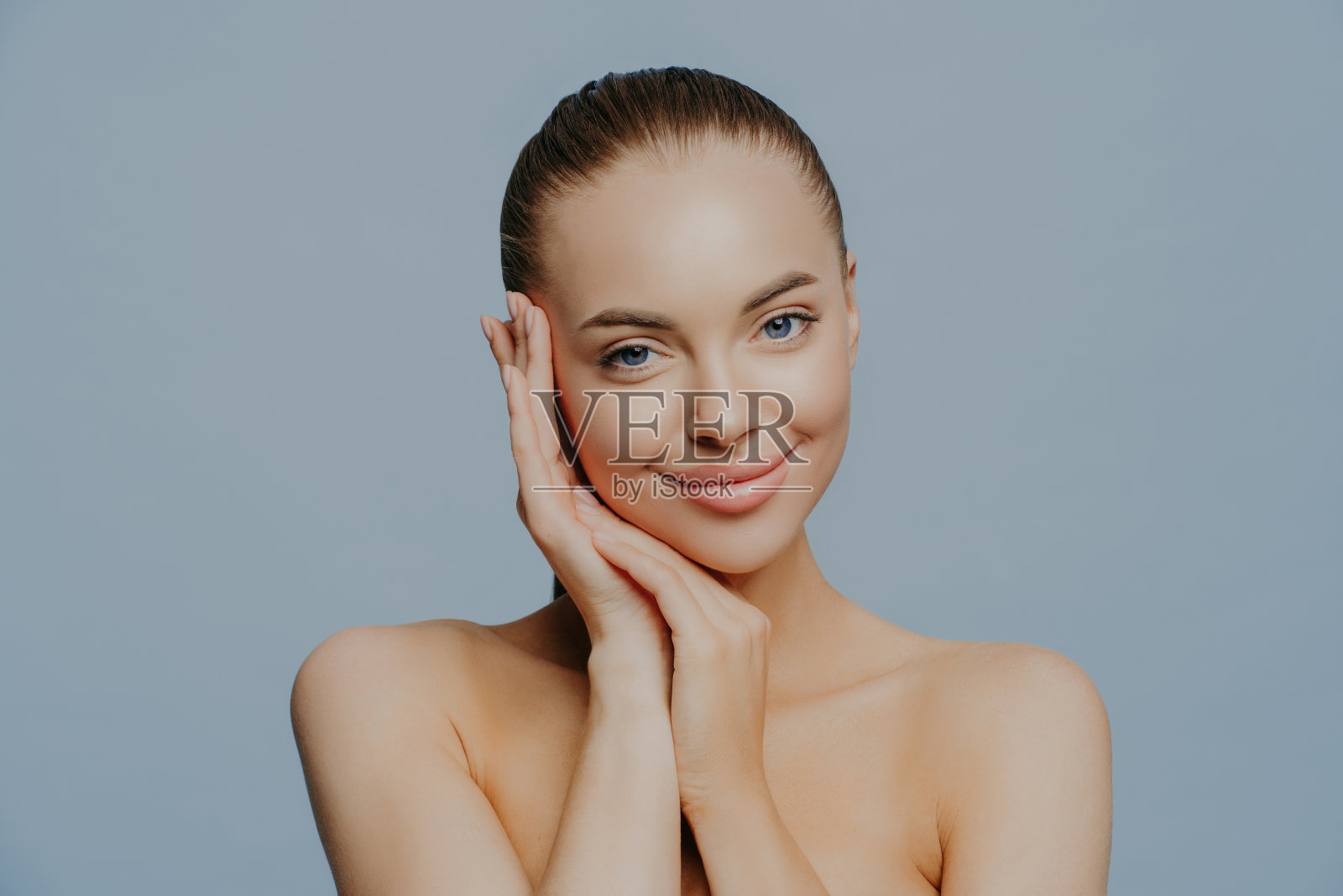 美女脸部肖像。美丽的水疗模特女孩完美清新干净的皮肤在蓝色的背景。黑发女性看着镜头。青春护肤理念。照片摄影图片