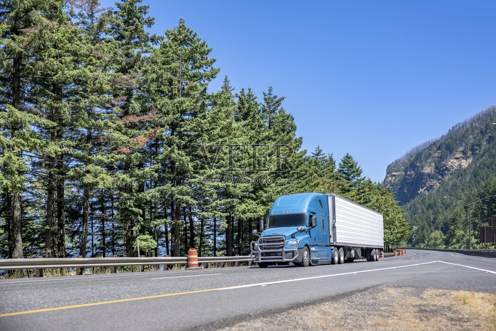 浅蓝色带格栅护栅的大卡车用冰箱半挂车运输货物，行驶在分岔交通线路的高速公路上照片摄影图片