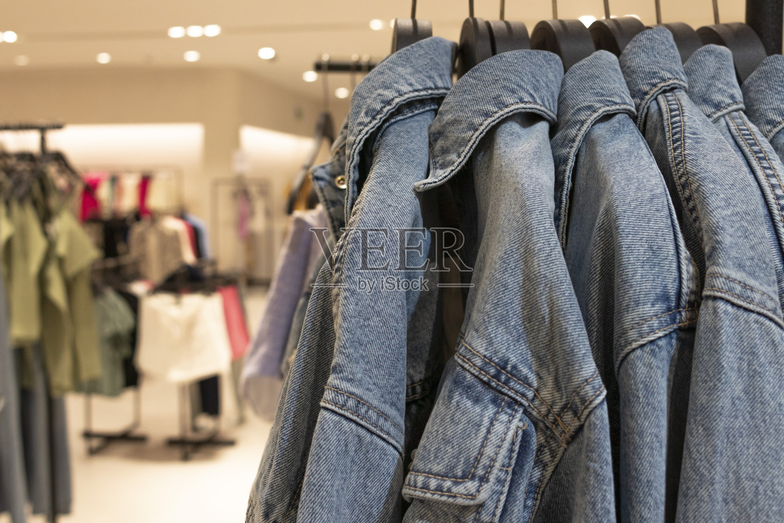 女性牛仔夹克挂在衣架上。散焦店背景。照片摄影图片
