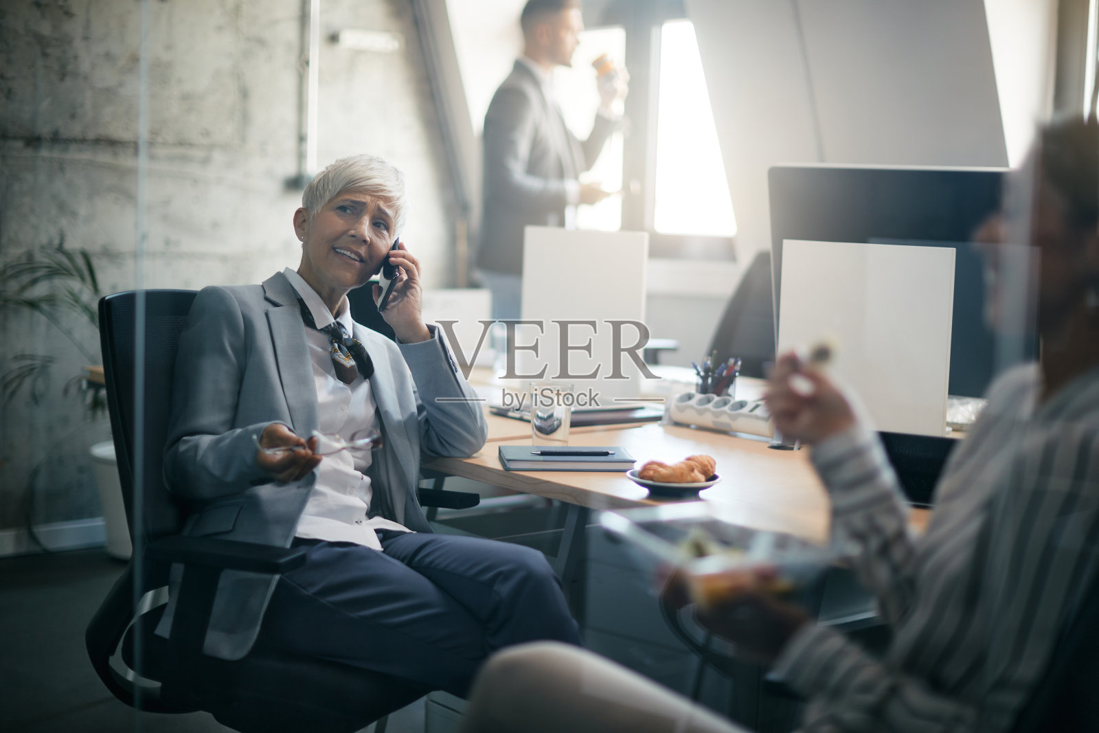 成熟的女商人在公司办公室工作时讲电话。照片摄影图片