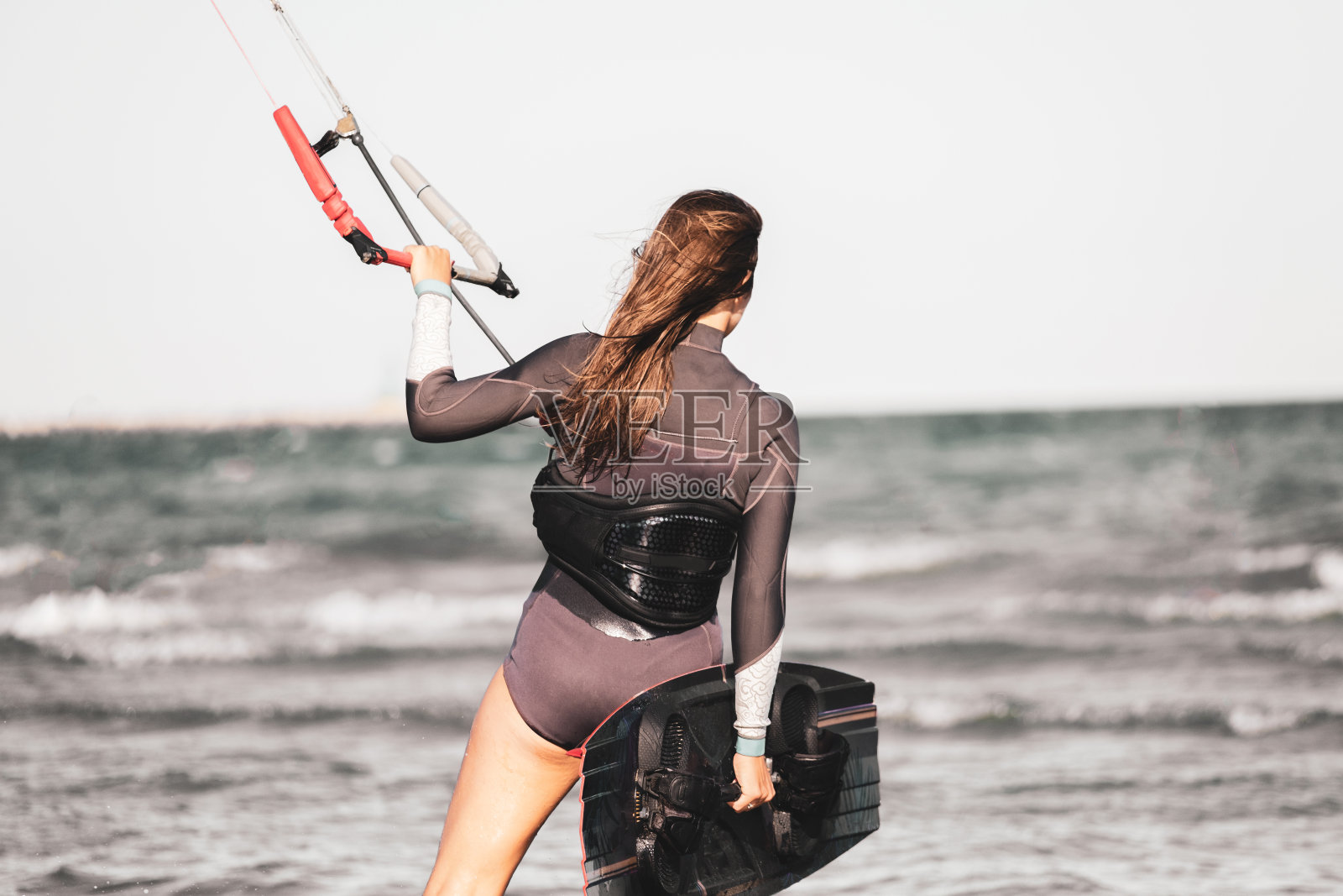 年轻美丽的运动女子准备在潜水服风筝冲浪在海滩海岸风筝-一个年轻的女孩风筝冲浪准备进入大海与她的板照片摄影图片
